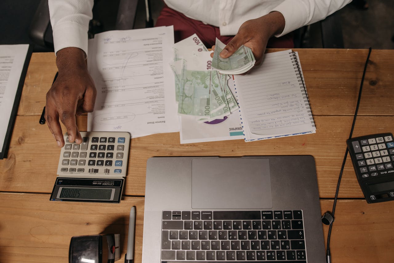 gallery-2 Close-up of a person counting cash with documents and a laptop in an office setting.
