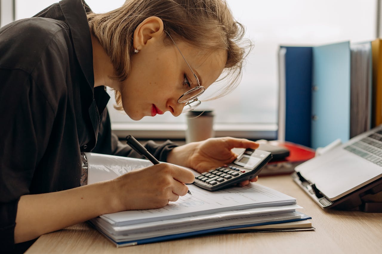 gallery-1 Young woman diligently working on accounting with a calculator and documents. Perfect for business and finance themes.