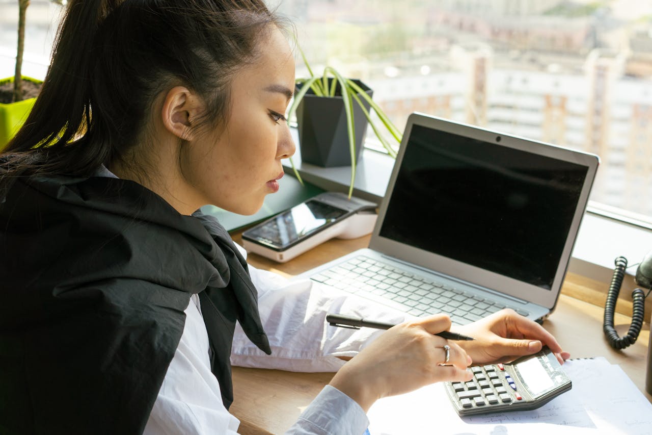 services-03 Asian woman working in a bright office, calculating finance on a desk with a laptop.